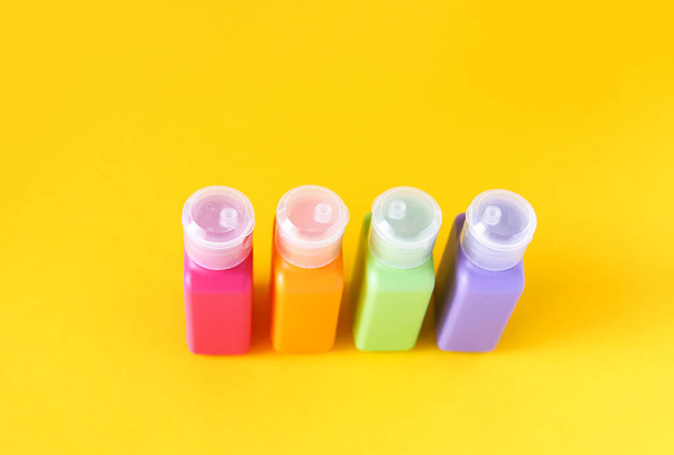 Πολύχρωμα πλαστικά μπουκάλια για προϊόντα περιποίησης του δέρματος σε έντονο κίτρινο φόντο - Φωτογραφία, εικόνα