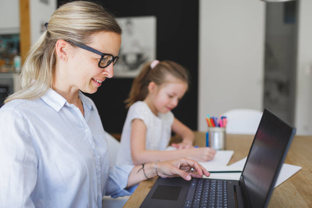 woman working with laptop from home office with her daughter homeschooling during corona crisis - Φωτογραφία, εικόνα