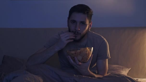 late night movie man watching tv eating chips bed - Materiał filmowy, wideo
