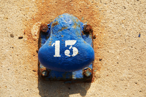 Blue rusty boat mooring with a number thirteen painted in white on a rough surface with a yellow texture - Photo, Image