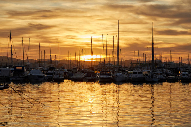 Many boats moored on the coast of the island of Ibiza with the sun setting on the horizon - Photo, Image