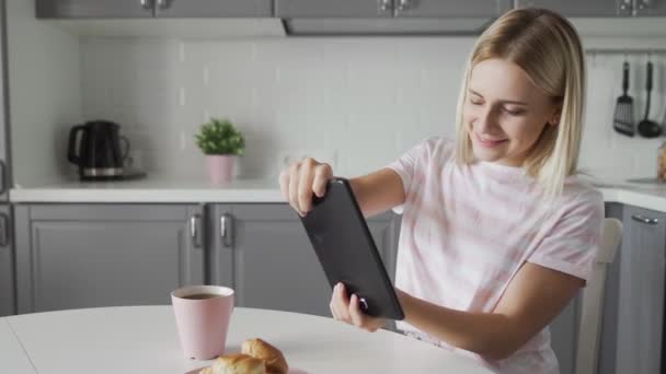 Attractive woman play video game on tablet device while having breakfast on her kitchen - Video