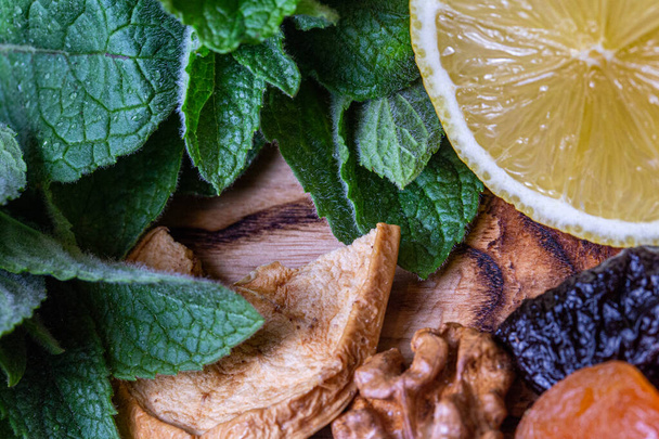 Natura morta alimentare in cucina con menta, limone, prugne secche, arachidi, mele secche e albicocche sul tagliere di legno
 - Foto, immagini