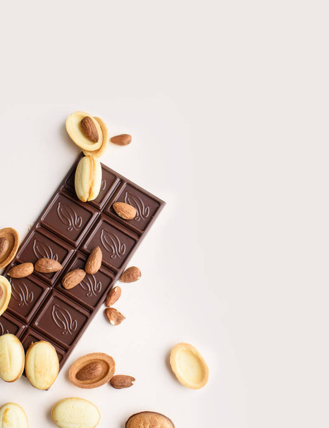 Een reep chocolade ligt op een lichte achtergrond met amandelen, walnoten, noten met gekookte gecondenseerde melk. Weergave van bovenaf, plaats voor tekst. - Foto, afbeelding