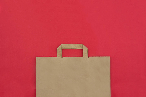 bruine papieren tas met handvatten op een rode achtergrond. bovenaanzicht - Foto, afbeelding