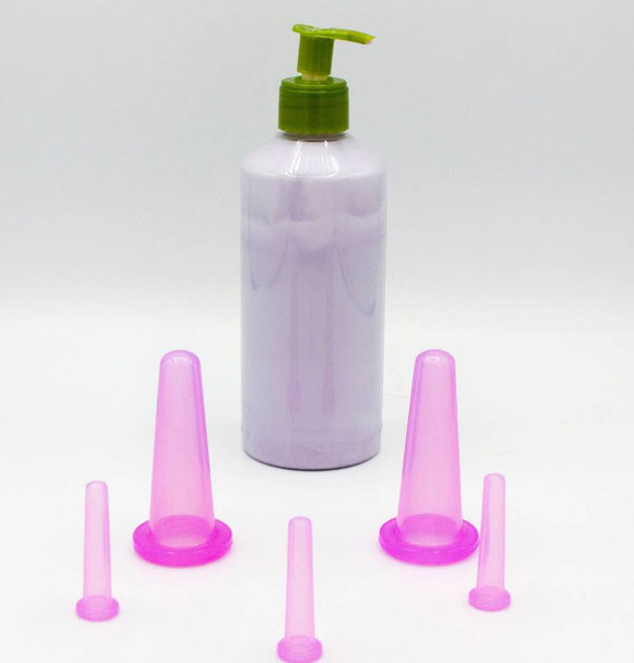 vijf roze cosmetische vacuümpotten voor lichaamsmassage en gezichtsmassage van verschillende maten gemaakt van siliconen en rubber met een flesje crème op witte achtergrond. Sluiten. - Foto, afbeelding