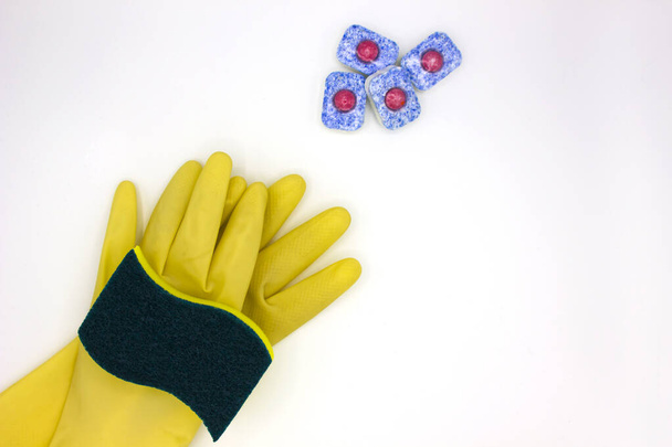 vaatwasmiddelen: spons, afwastablet, gele handschoenen op witte achtergrond. Bovenaanzicht, van dichtbij. Schoon huis- en handverzorgingsconcept - Foto, afbeelding