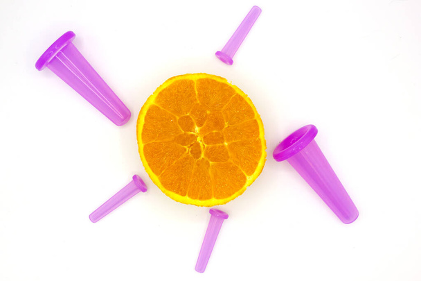 Top view of the orange like a sun with pink vacuum ribber cans on white background. Body care treatments home spa concept. Top view. Space for text. - Photo, Image