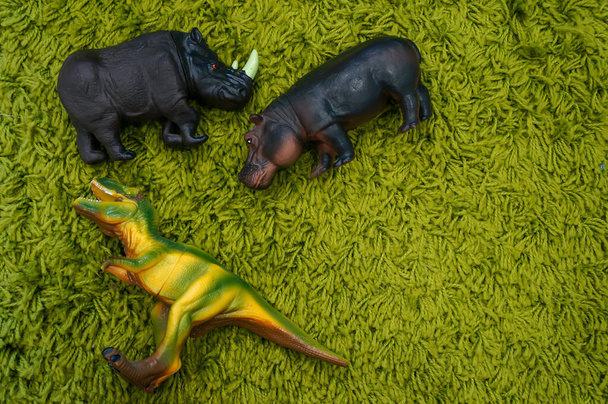  Παιδικό παιχνίδι δεινόσαυρος ιπποπόταμος και ρινόκερος σε ένα πράσινο χαλί με θέση για το κείμενό σας. - Φωτογραφία, εικόνα
