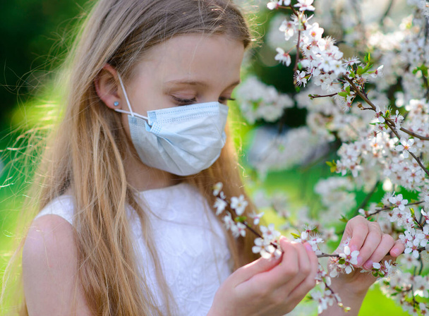 Tiener meisje met medisch masker in de lente bloeiende tuin. Concept sociale afstand, preventie van coronavirus. - Foto, afbeelding