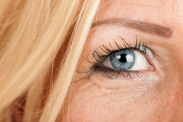 Nahaufnahme des rechten Auges einer blonden, blauäugigen Frau mittleren Alters. - Foto, Bild