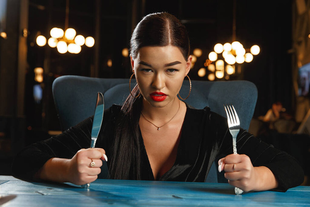 Une fille affamée attend de la nourriture. Tenant un couteau et une fourchette
 - Photo, image