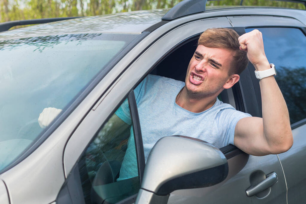Angry aggressive guy, young emotional irritated man driver screaming, shouting, yelling while driving car, threatening with a fist from automobile window. Driving anger negative emotion, agression - Photo, image