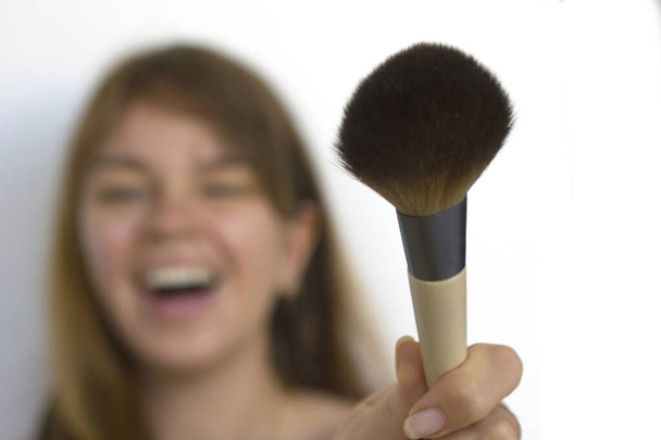 Jovem mulher bonita rindo com maquiagem escova no fundo branco. escova focada
 - Foto, Imagem