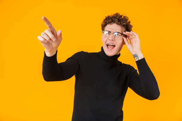 Image of young excited man in eyeglasses pointing finger aside isolated over yellow background - Фото, зображення