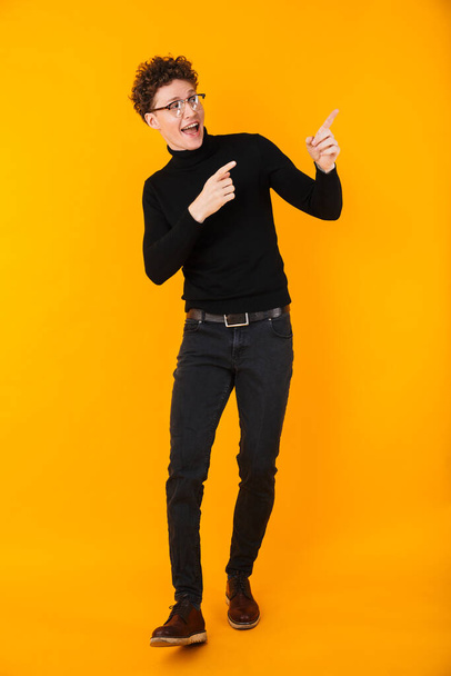 Image of young excited man in eyeglasses pointing fingers aside isolated over yellow background - Photo, Image