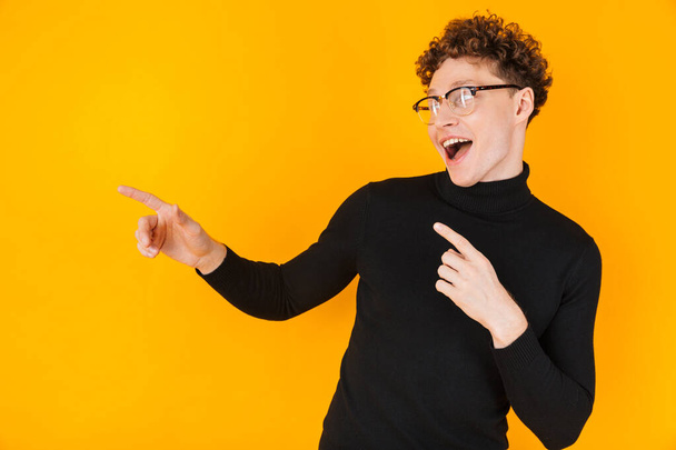 Image of young excited man in eyeglasses pointing fingers aside isolated over yellow background - Valokuva, kuva