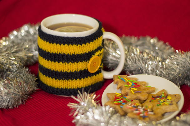 Taza en punto cubierta con té y galletas de Navidad
 - Foto, imagen