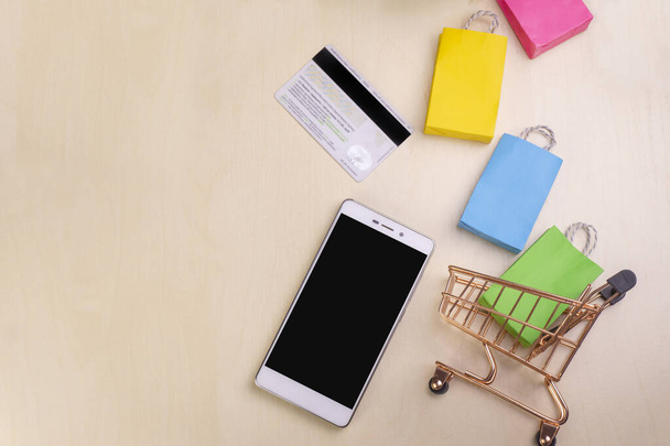 smartphone στέκεται, πιστωτική κάρτα, τσάντες, κουτιά σε ξύλινο τραπέζι με φυτά στο παρασκήνιο - Φωτογραφία, εικόνα