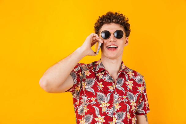 Image of young cheerful man talking on cellphone and smiling isolated over yellow background - Foto, imagen
