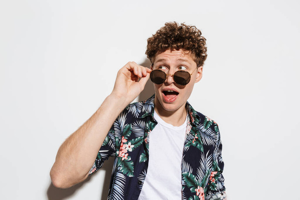 Image of young excited man in sunglasses expressing surprise at camera isolated over white background - Foto, Bild