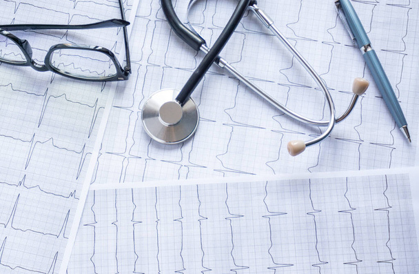 kardiogram se stetoskopem, perem, lupou, pilulkami a brýlemi ležel na stole - Fotografie, Obrázek