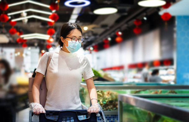 Koronavirüs salgını sırasında virius yayılmasını önlemek için maske ve eldiven takan Asyalı bir kadın markette alışveriş yapıyor. - Fotoğraf, Görsel