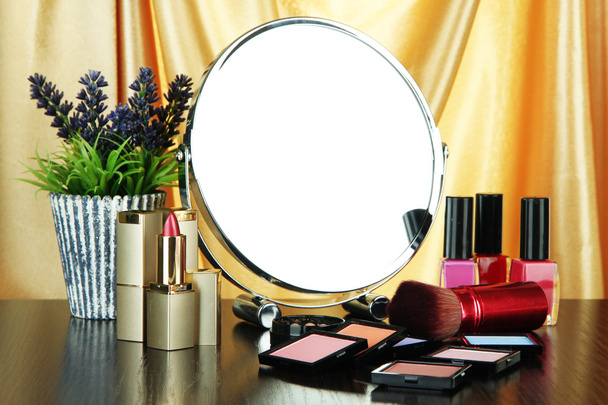 Round table mirror with cosmetics and flowers on table on fabric background - Photo, image