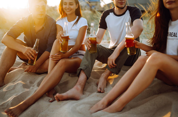 Group of young friends sitting together at the beach talking and drinking beers at sunset. Summer holidays, vacation, relax and lifestyle consept. - Φωτογραφία, εικόνα