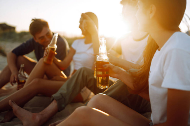 Group of young friends sitting together at the beach talking and drinking beers at sunset. Summer holidays, vacation, relax and lifestyle consept. - Foto, Imagen