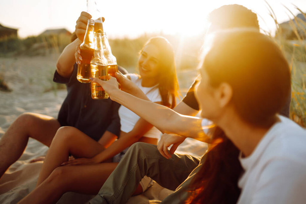 Group of young friends sitting together at the beach talking and drinking beers at sunset. Summer holidays, vacation, relax and lifestyle consept. - Foto, immagini
