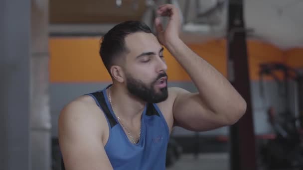 Portrait of tired satisfied Middle Eastern sportsman sighing, wiping forehead and drinking water. Young handsome man resting after training in gym. Active lifestyle, sport, fitness, health. - Filmagem, Vídeo