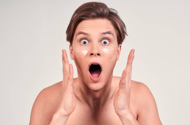 Surprised, shocked young naked man, a young man, blond with blue eyes, wears patches on his face to moisturize the skin, shocked by the effect of rejuvenation. - Foto, Imagen