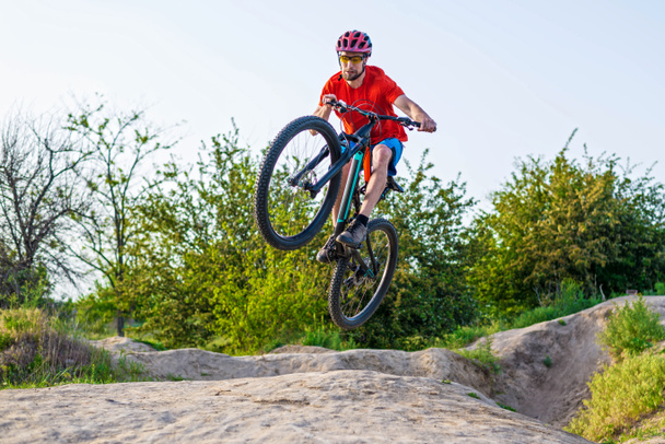 Extremfahrrad-Konzept, Radfahrer springen auf einem Mountainbike. Radfahrer in leuchtend orangefarbenem T-Shirt und Helm. - Foto, Bild