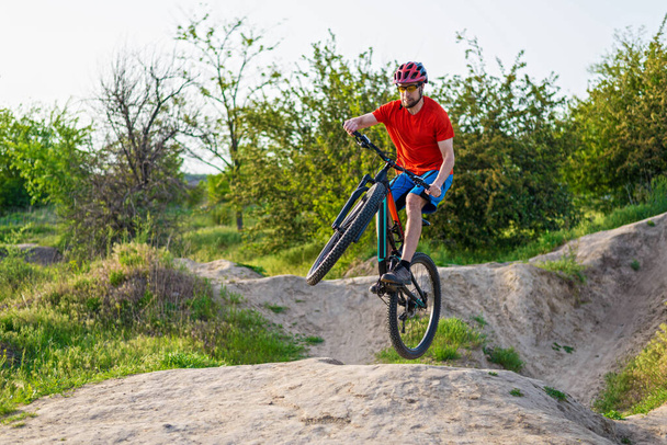 Professional cyclist in a bright T-shirt performs a jump. Extreme sport. Cyclist on a mountain bike. - Zdjęcie, obraz