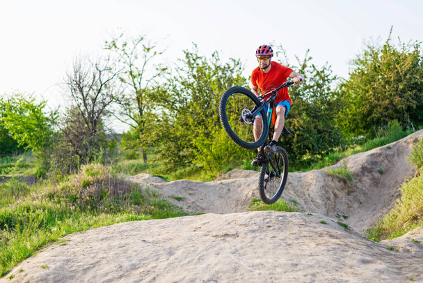 Professionele fietser in een helder T-shirt doet een sprong. Extreme sport. Fietser op een mountainbike. - Foto, afbeelding