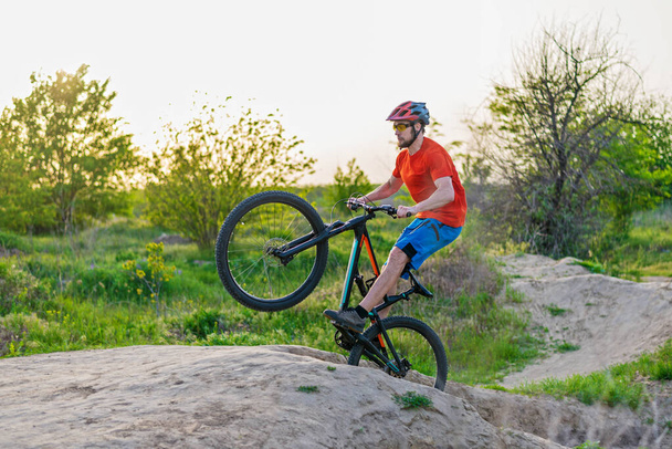 Extreme pyöräily käsite, pyöräilijä hyppää maastopyörä. Pyöräilijä kirkkaan oranssissa t-paidassa ja kypärässä
. - Valokuva, kuva