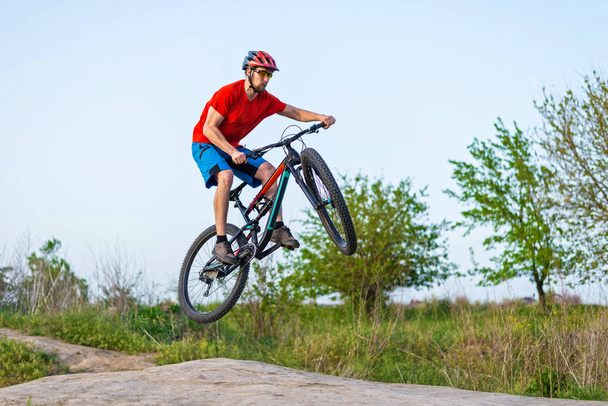 Ακραία έννοια ποδηλασία, ποδηλάτης άλμα σε ένα ποδήλατο βουνού. Ποδηλάτης σε ένα φωτεινό πορτοκαλί t-shirt και κράνος. - Φωτογραφία, εικόνα