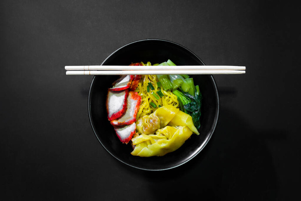 Egg noodle and wonton with red roast pork and green vegetables in black background, Image from the top view - Photo, Image