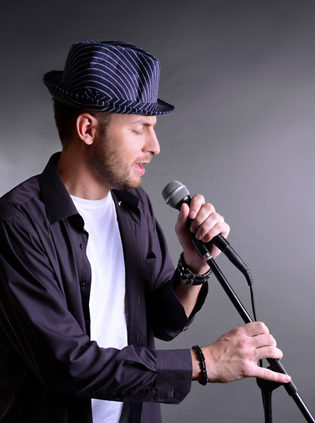 Young musician singing, on gray background - Zdjęcie, obraz