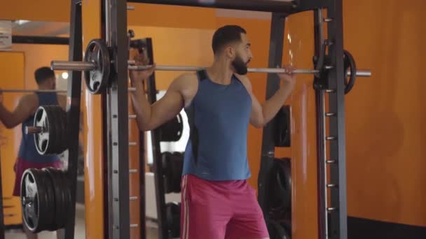 Young sportive Middle Eastern man lifting weights in gym. Portrait of handsome sportsman training in sports club. Health, lifestyle, fitness, strength, muscular build. - Video