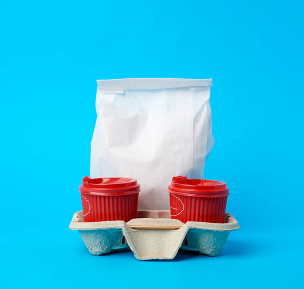 rood wegwerp papieren bekers in de schaal en een volledig witte papieren zak op een blauwe achtergrond, voedselleveringsconcept, online bestellen - Foto, afbeelding