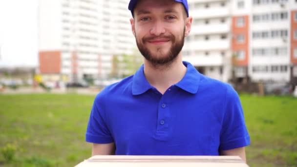 Portrét mladého atraktivního mužského kurýra doručovatele na pozadí budovy - Záběry, video