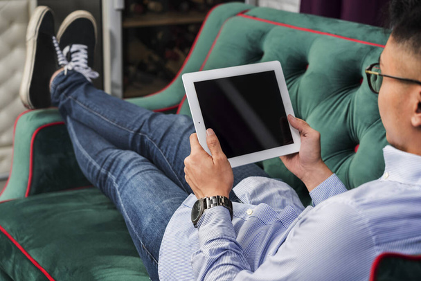 Man using a digital tablet on a couch - Фото, изображение