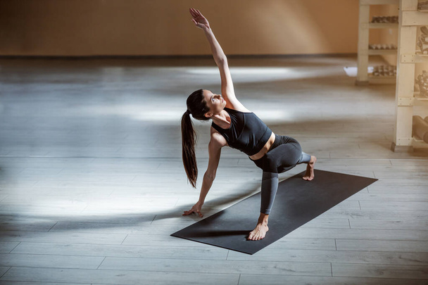 Slim αφιερωμένο κορίτσι yogi στέκεται στο χαλί στο Lunge με το χέρι Extended Up πόζα γιόγκα. Yoga studio εσωτερικό. - Φωτογραφία, εικόνα