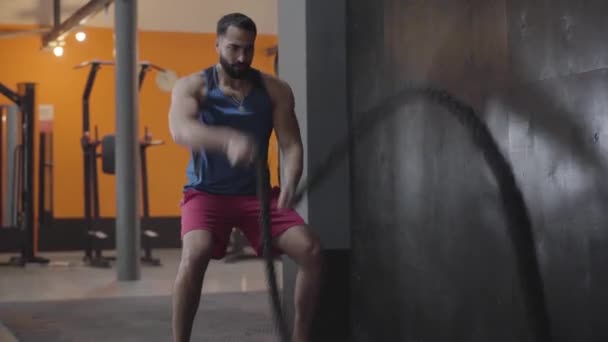 Ισχυρή μυώδης αθλητής κάνει crossfit άσκηση στο γυμναστήριο. Ευρεία βολή ενός όμορφου άντρα της Μέσης Ανατολής που χρησιμοποιεί σχοινιά για εκπαίδευση αντοχής. Αθλητισμός, τρόπος ζωής, υγεία, προπόνηση. - Πλάνα, βίντεο