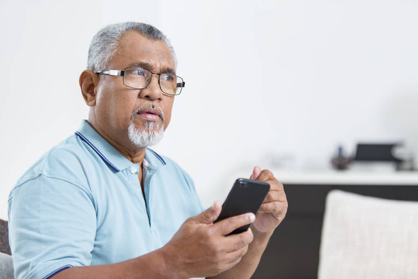 Senior man is thinking while holding a smartphone - Photo, image
