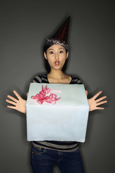 Frau mit Partyhut hält ein großes Geschenk in der Hand und sieht überrascht aus - Foto, Bild