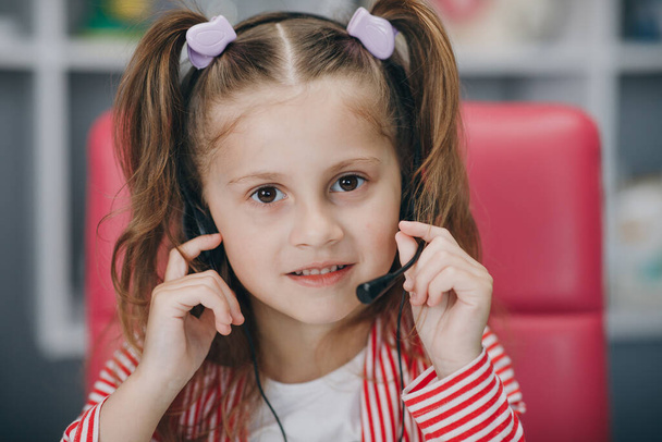 Portrait of smiling little girl wearing headphones. Happy small preschooler child in earphones have fun. Studying online on quarantine. - 写真・画像