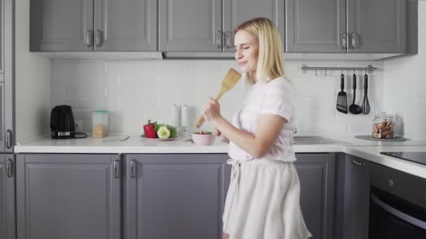Happy aktivní legrační mladá žena drží dřevěné špachtle mikrofon zpěv karaoke píseň tanec poslech hudba vaření v kuchyni - Záběry, video